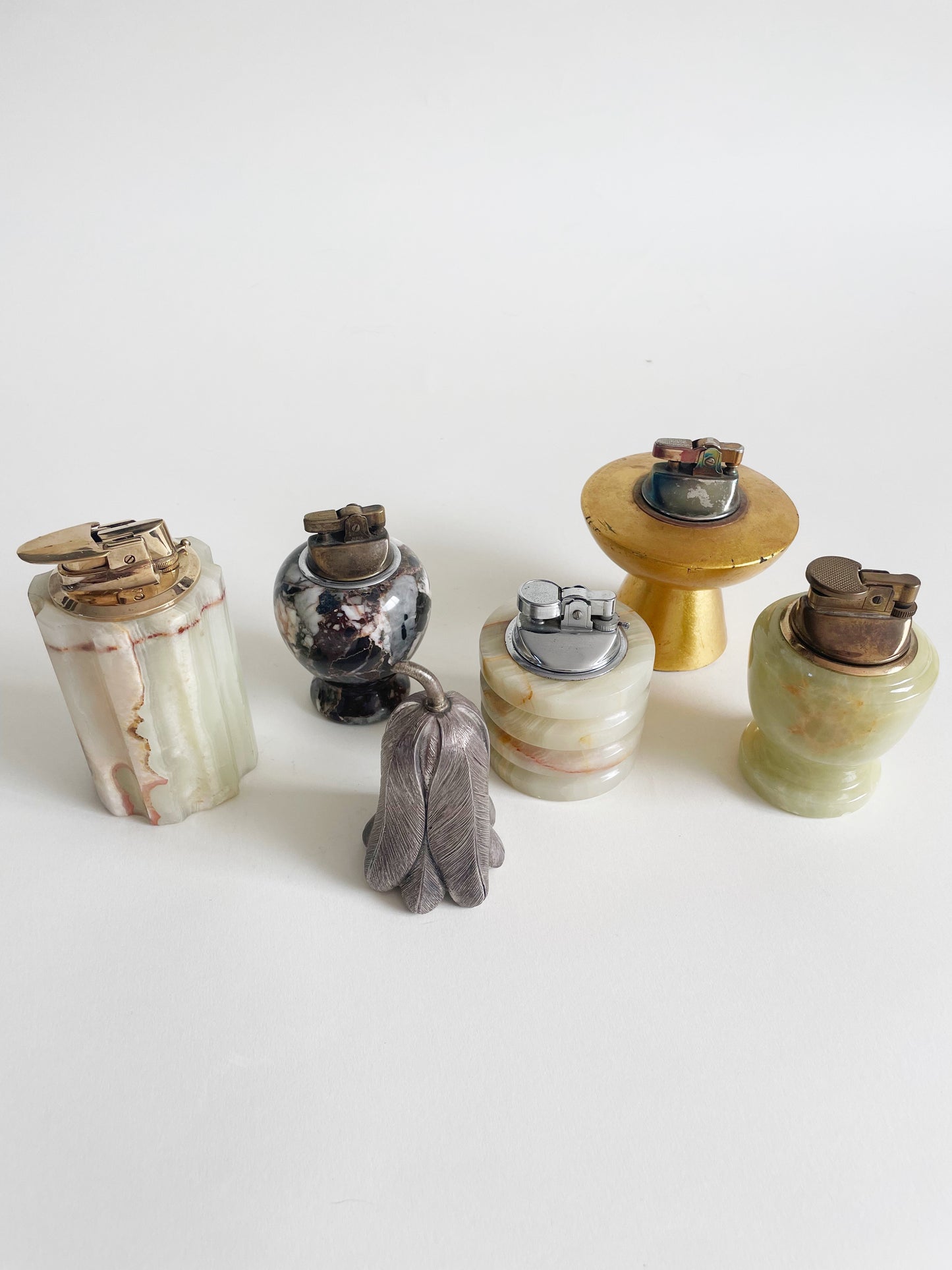 A collection of vintage lighters on a white background, featuring various shapes and materials, including metal and stone designs.