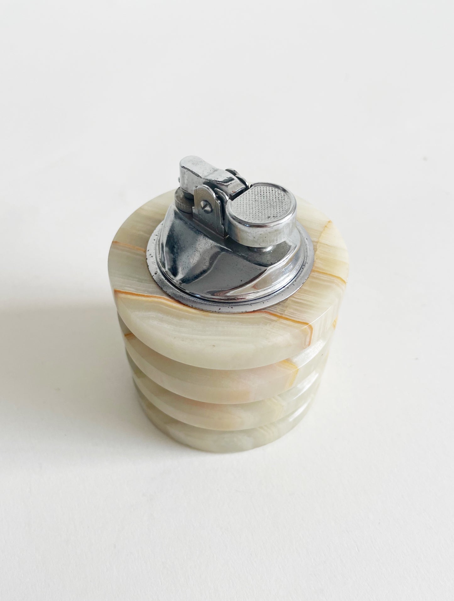 A vintage tabletop lighter with a silver top and a layered stone body in shades of beige and cream, set against a white background.