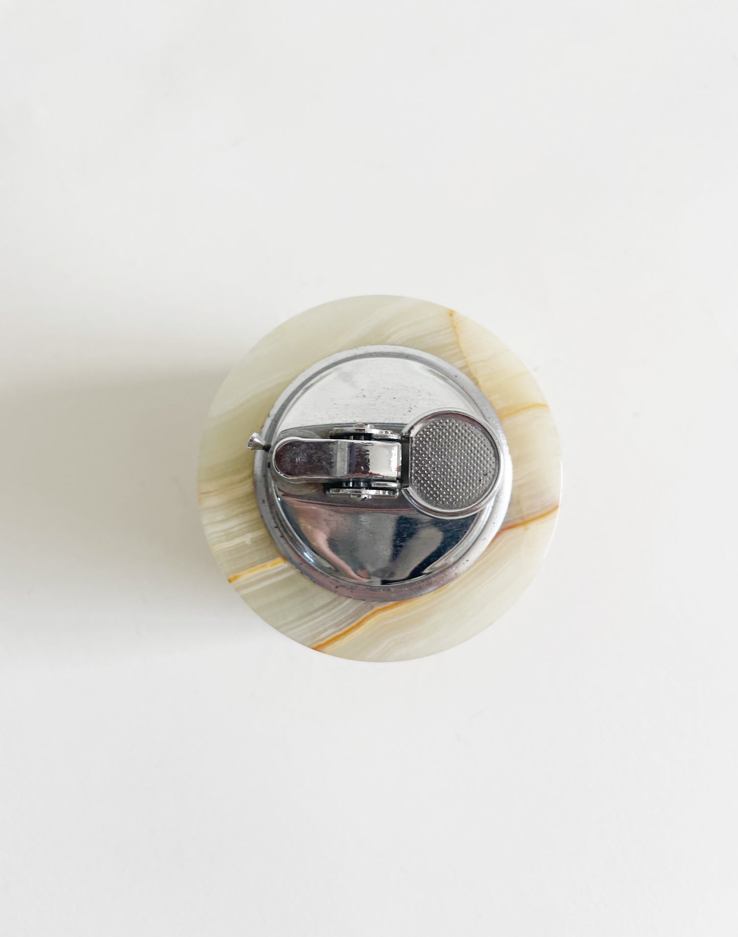 Top view of a round, silver metal lighter with a stone-like base, featuring a smooth surface and beige veining, set against a white background.