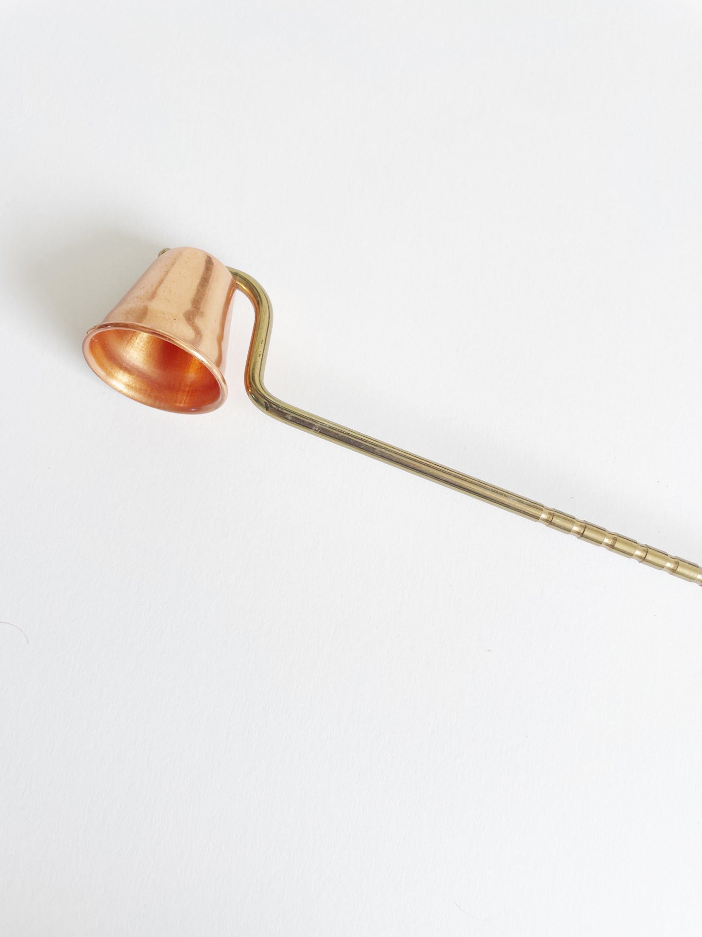 Copper candle snuffer with a long brass handle on a white background.