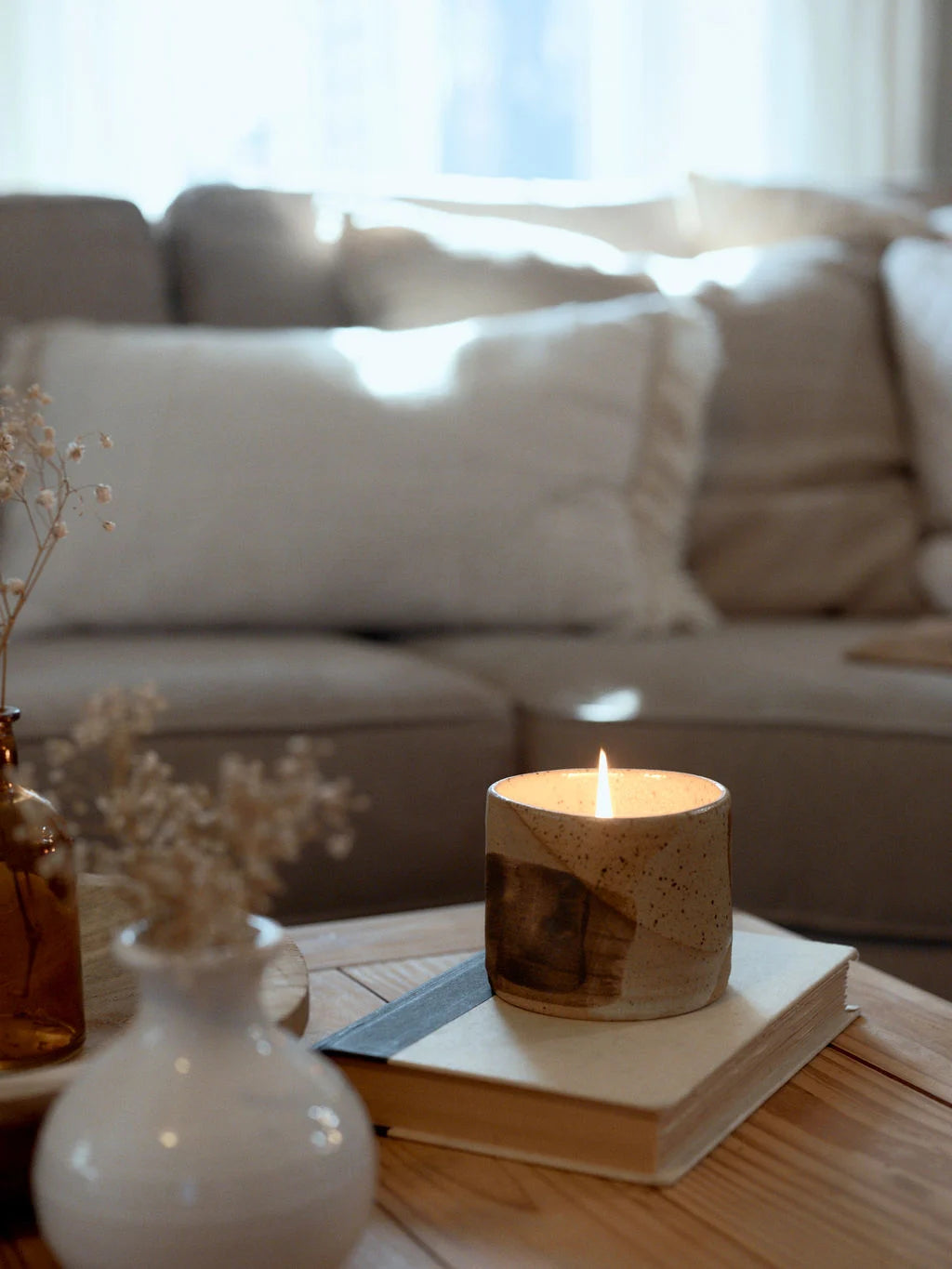 A ceramic bowl painted natural, earthy colors holds a lit bergamot, vanilla and coconut candle