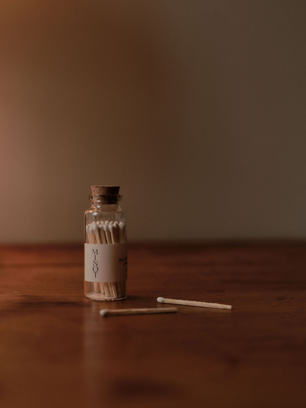 A beautiful, tiny glass jar of MINOT safety matches with a cork top and two loose matches on a table