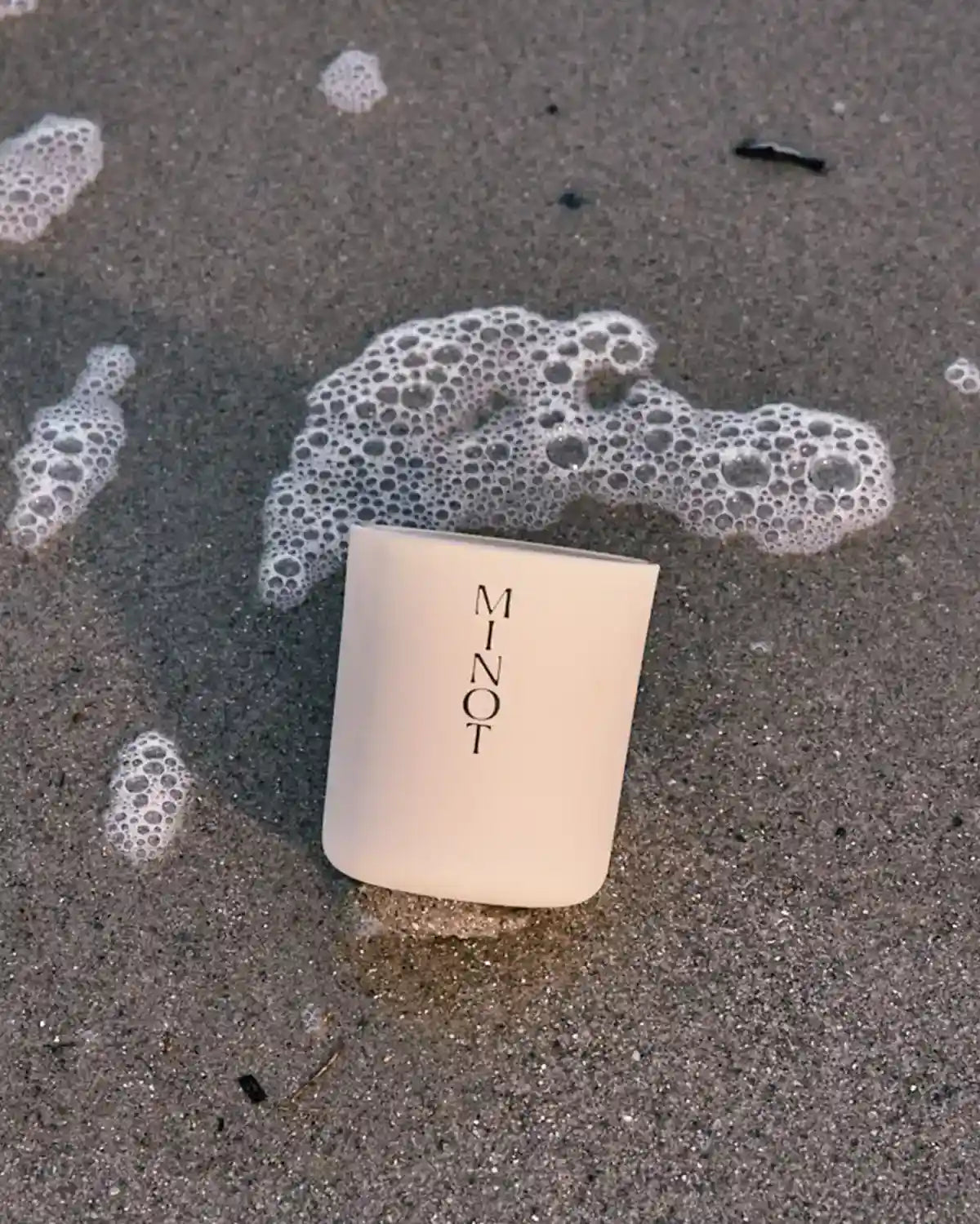 The minimalist candle Atmosphere is on wet beach sand, smelling of coconut, almonds and sandalwood