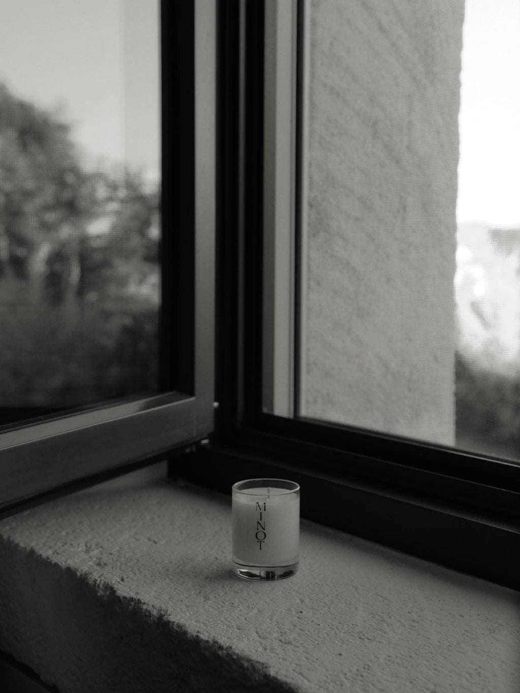 The Dusk Mini small travel candle sits in front of an open window, emanating tranquil spa scents