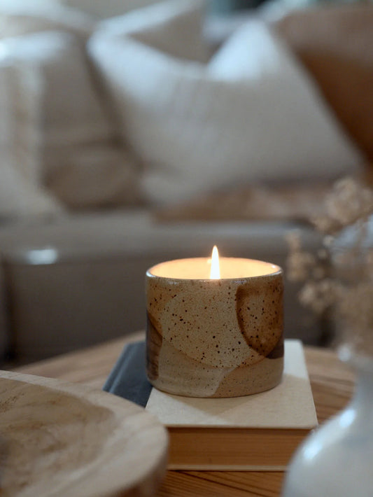 On top of a book sits a handmade, glazed ceramic vessel holding a lit soy candle for Mother's Day
