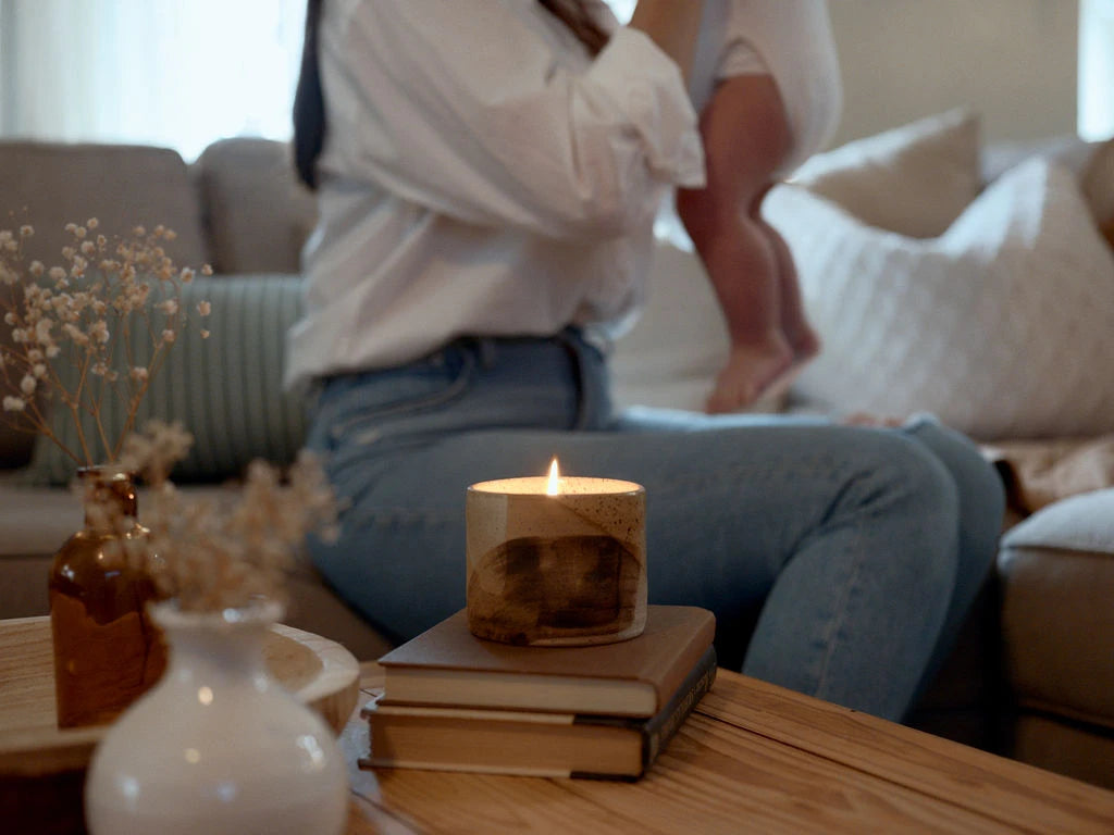 A candle flickers in a glazed ceramic bowl while a mother embraces her infant in the background