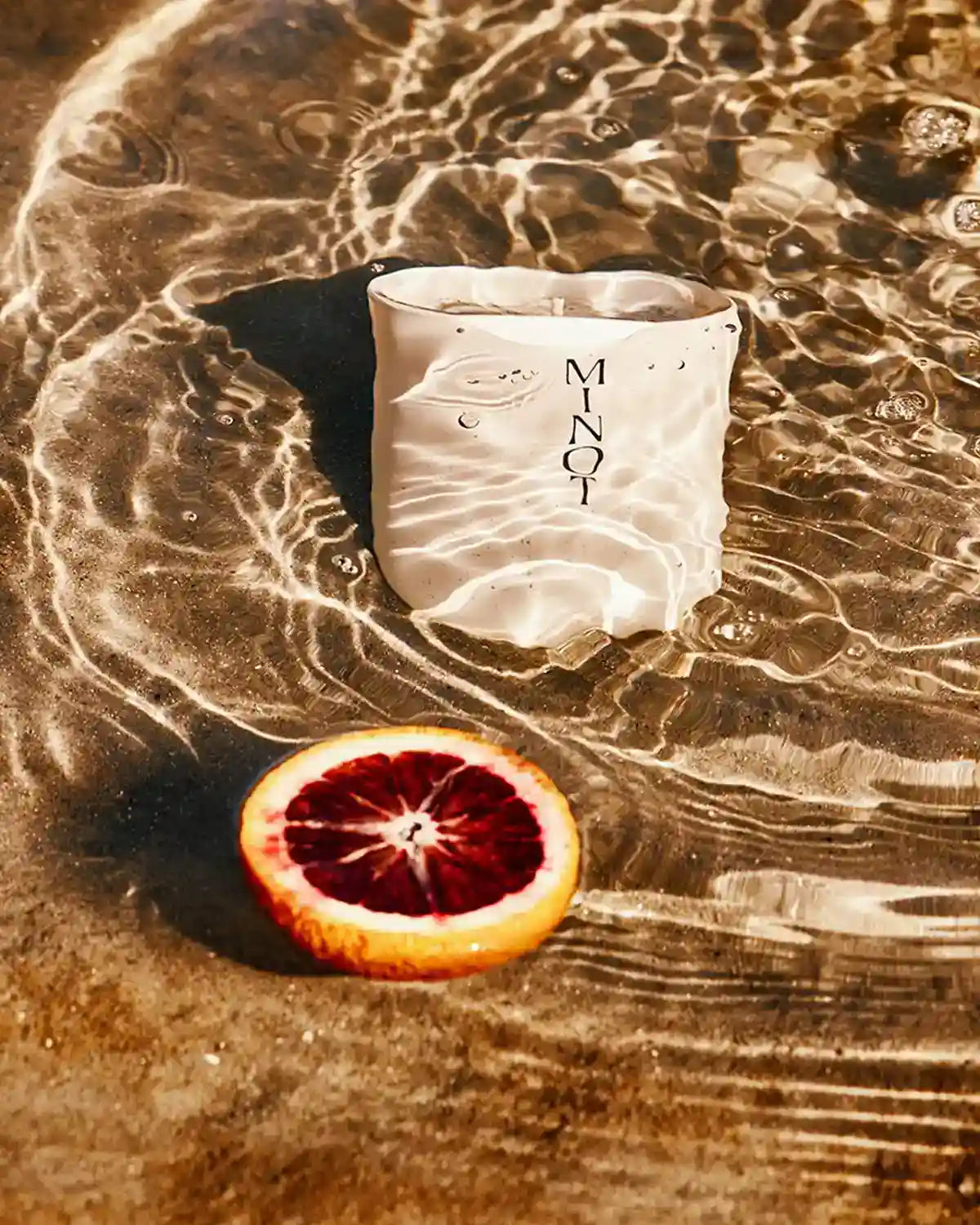 The eco-friendly, non-toxic Luna candle shimmers underwater next to a slice of citrus