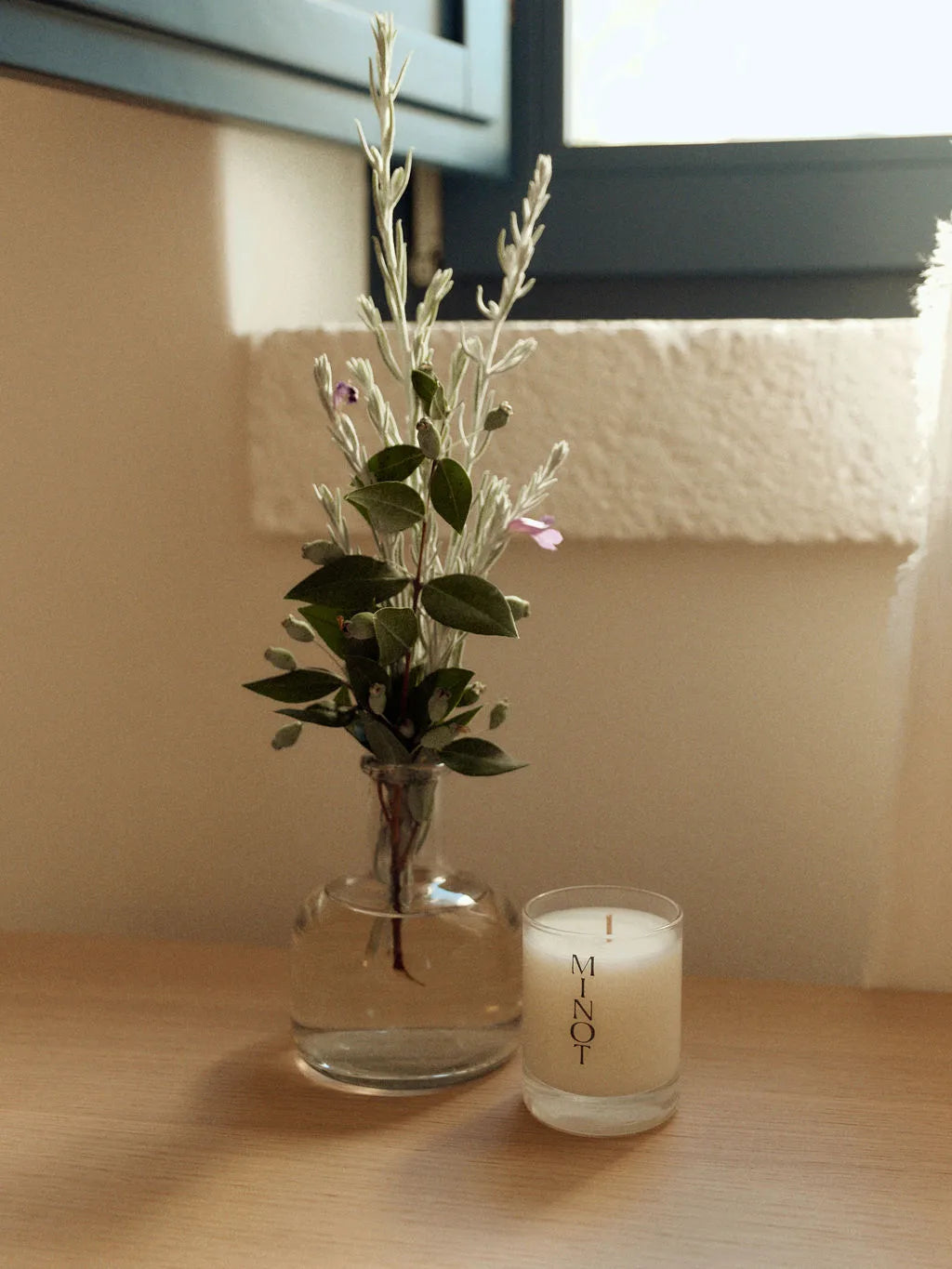 The eco-friendly Luna Mini candle sits next to a small bouquet of soft greenery and purple flowers