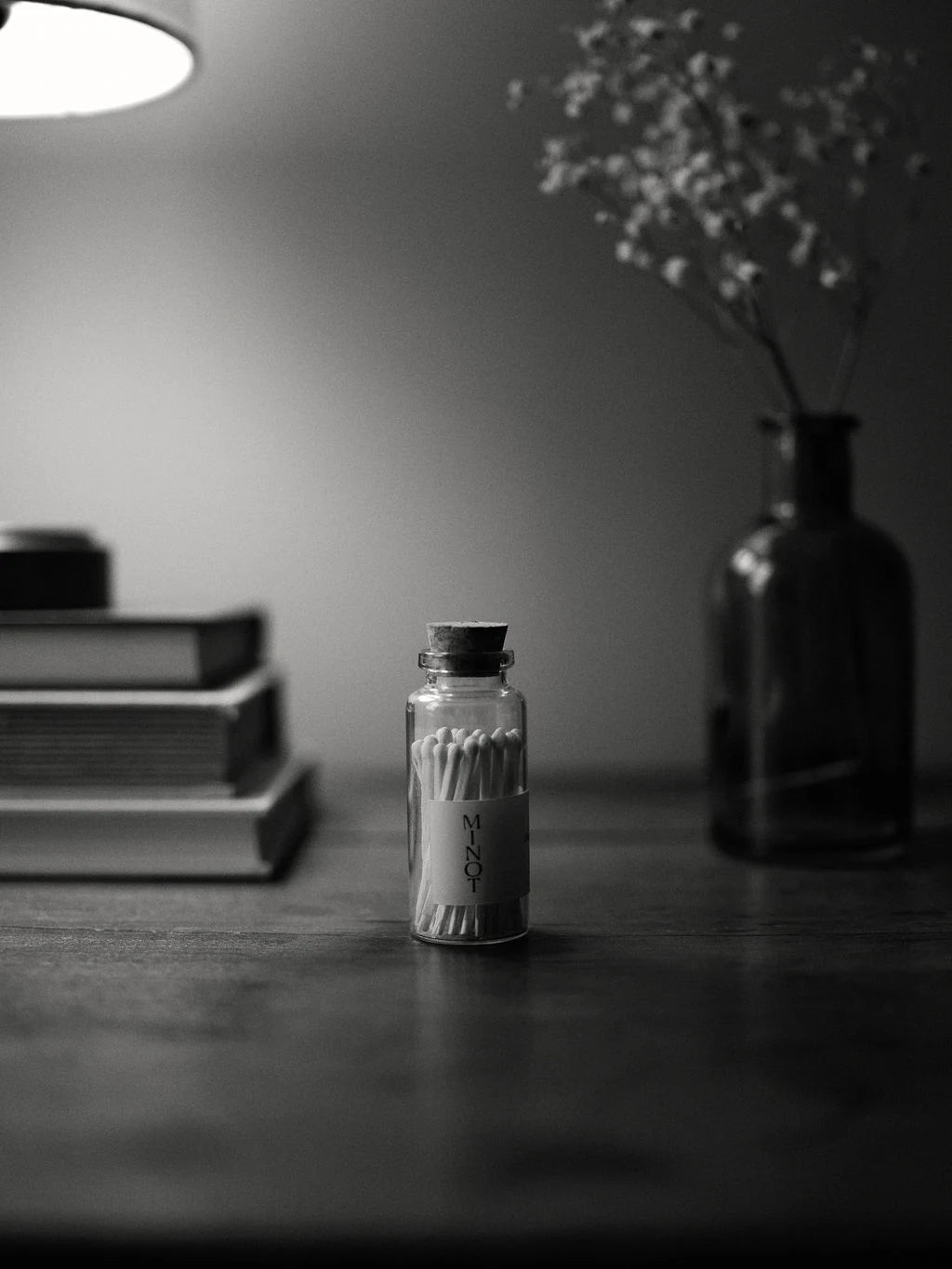 Grayscale MINOT matches in a small glass jar with a cork top sit next to books and dried flowers