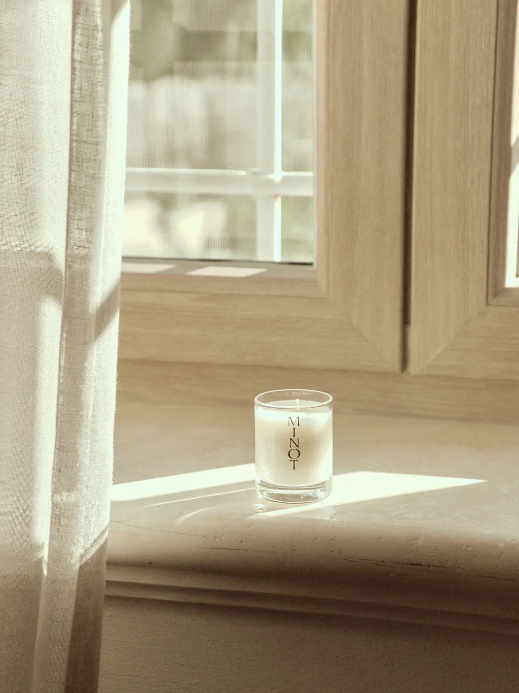 The Atmosphere Mini candle embodies the minimalist aesthetic sitting on a pale wooden windowsill