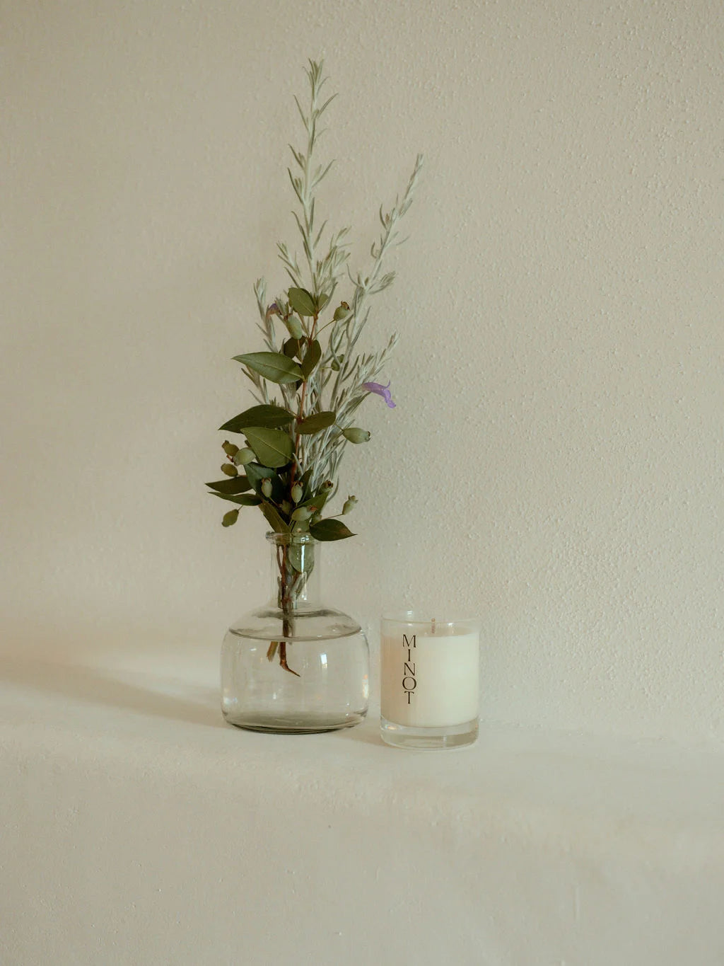 The minimalist Summit Mini candle sits next to a small bouquet of soft greenery and purple flowers