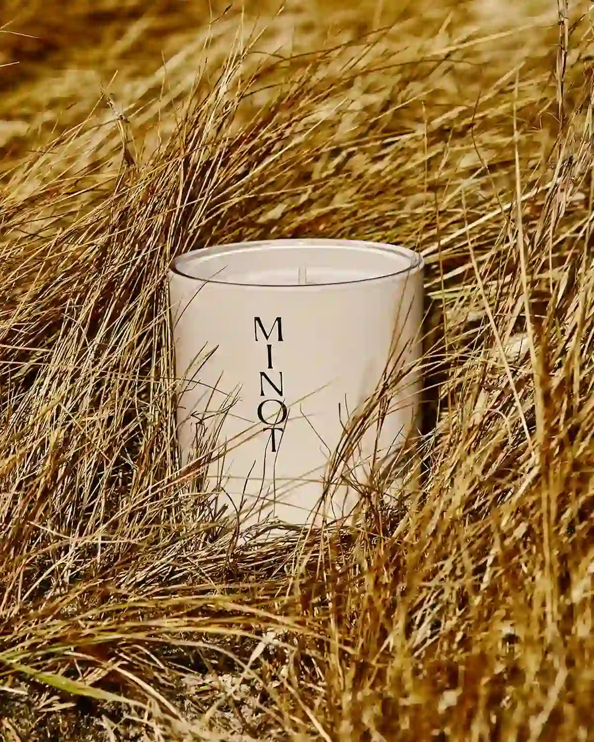 The Wild Meadow candle, surrounded by tan grasses, offers floral notes of lilac and honeysuckle